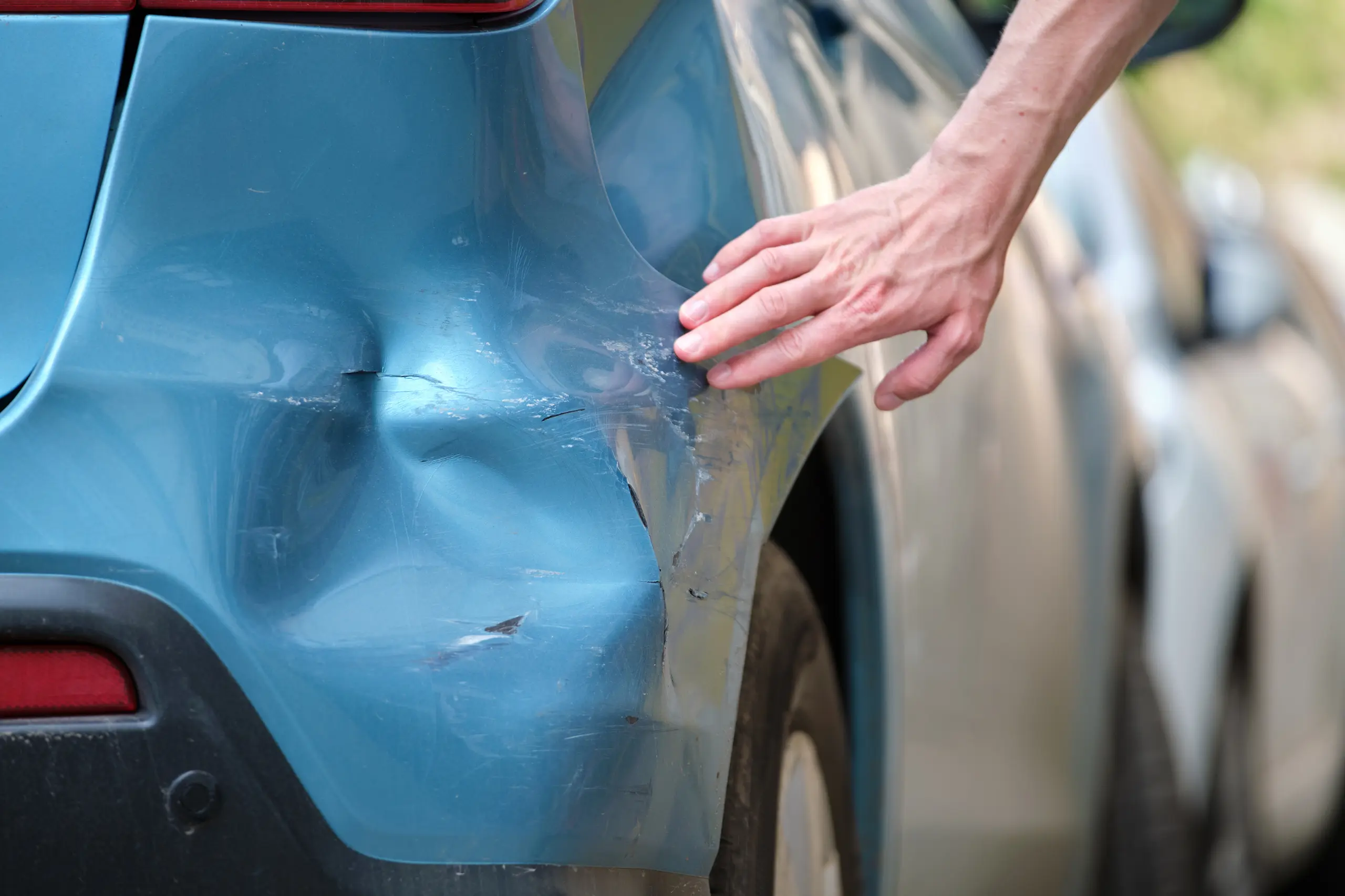 driver-hand-examining-dented-car-with-damaged-fend