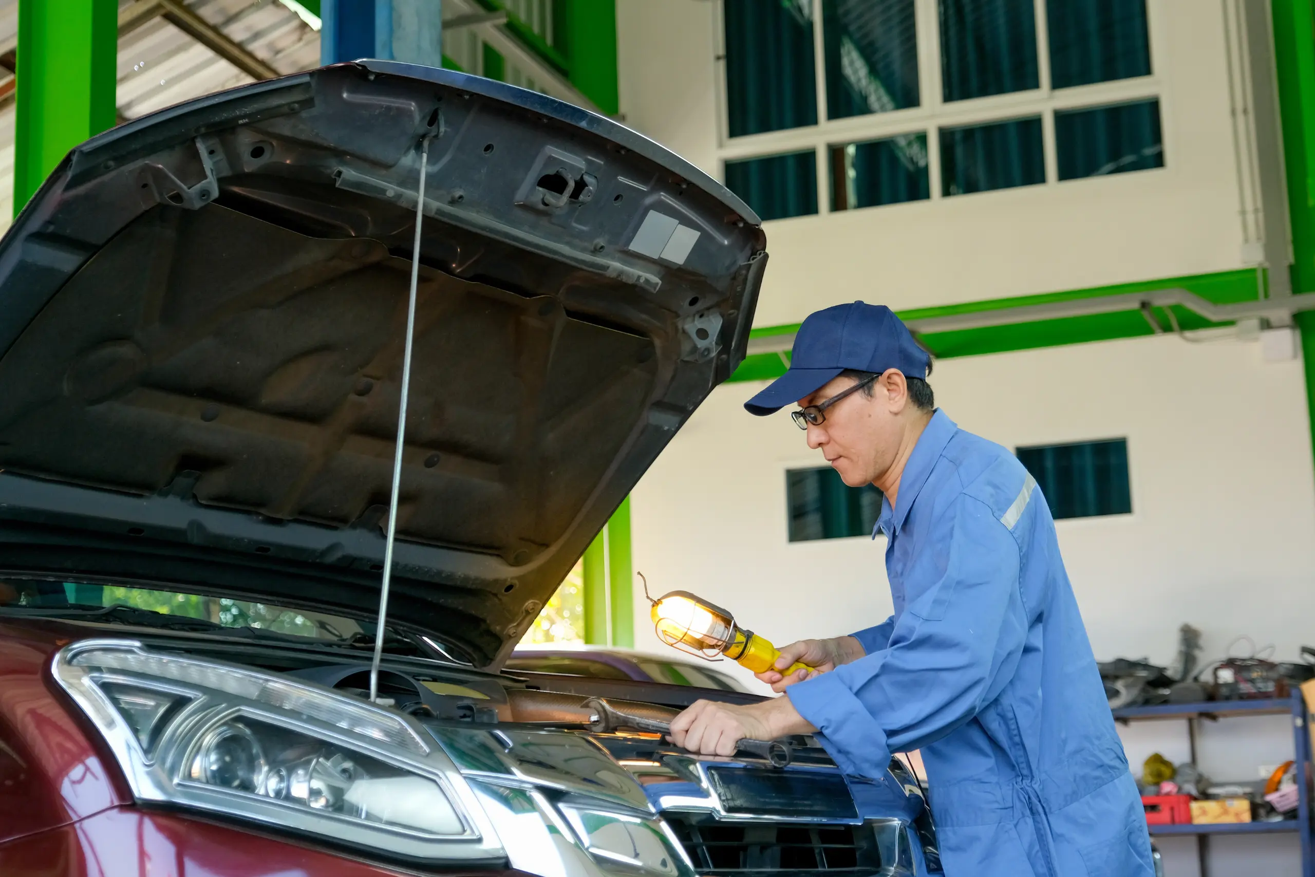 asian-automotive-mechanic-with-blue-uniform-checking-in-hood-of-car